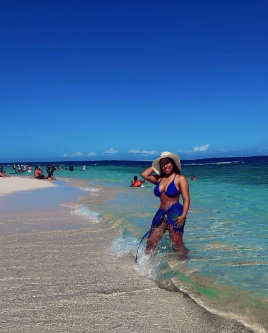 Woman in a blue bikini and sun hat smiling at the beach